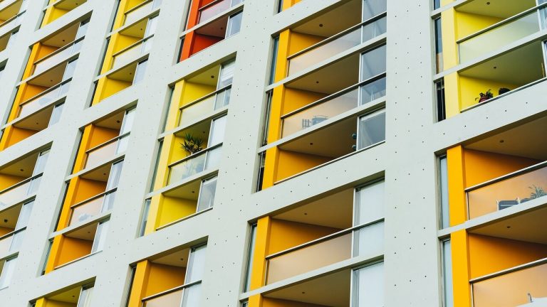 Facciata di un condominio con balconi vetrati e pareti colorate di giallo e arancione.